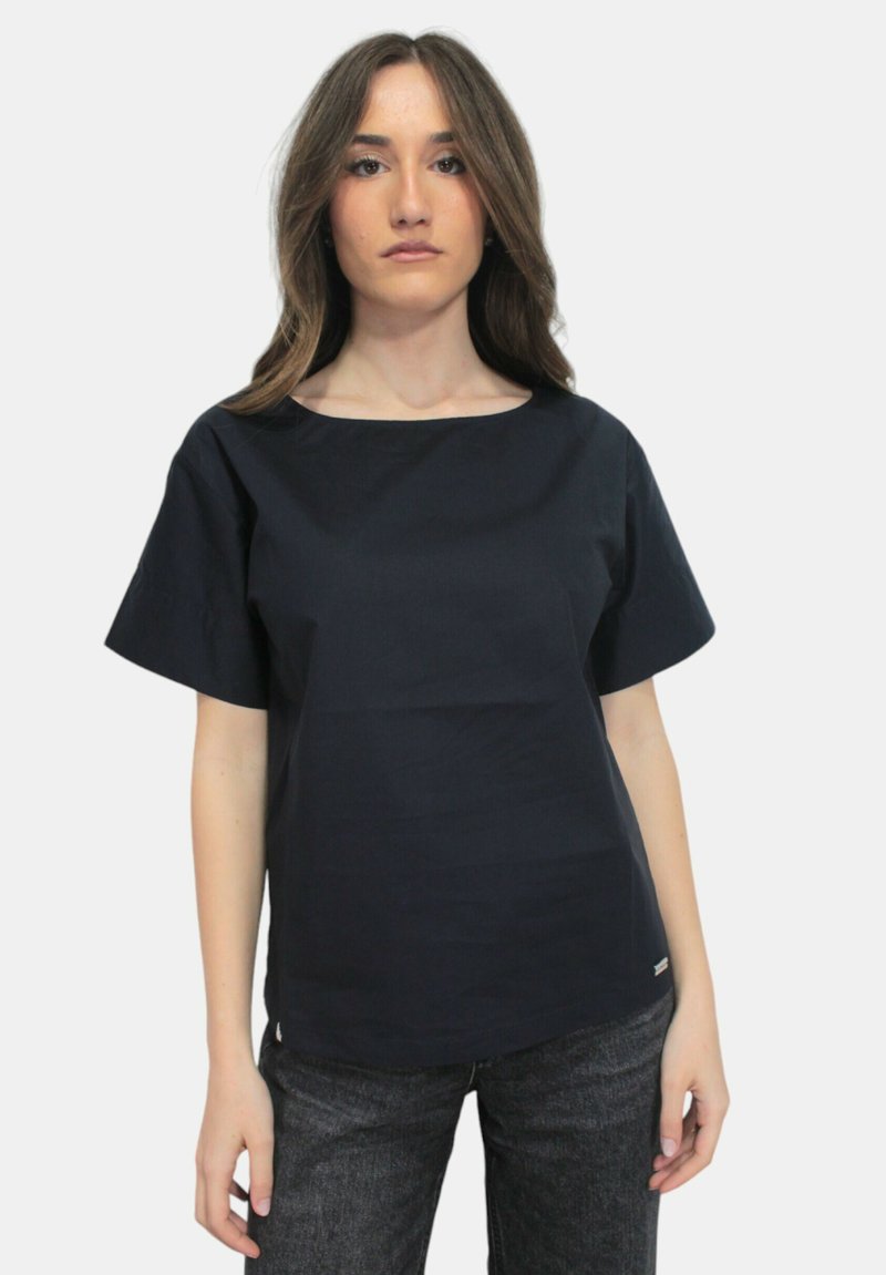 Top blu navy a maniche corte con scollatura rotonda, realizzato in tessuto liscio. Abbinato a jeans scuri e testurizzati con dettagli di branding minimi.