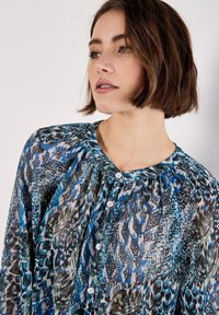 Fluffig blus med knappar i en blå och grön abstrakt mönster, genomskinligt tyg, plisserad design och rund halsringning med knappar.
