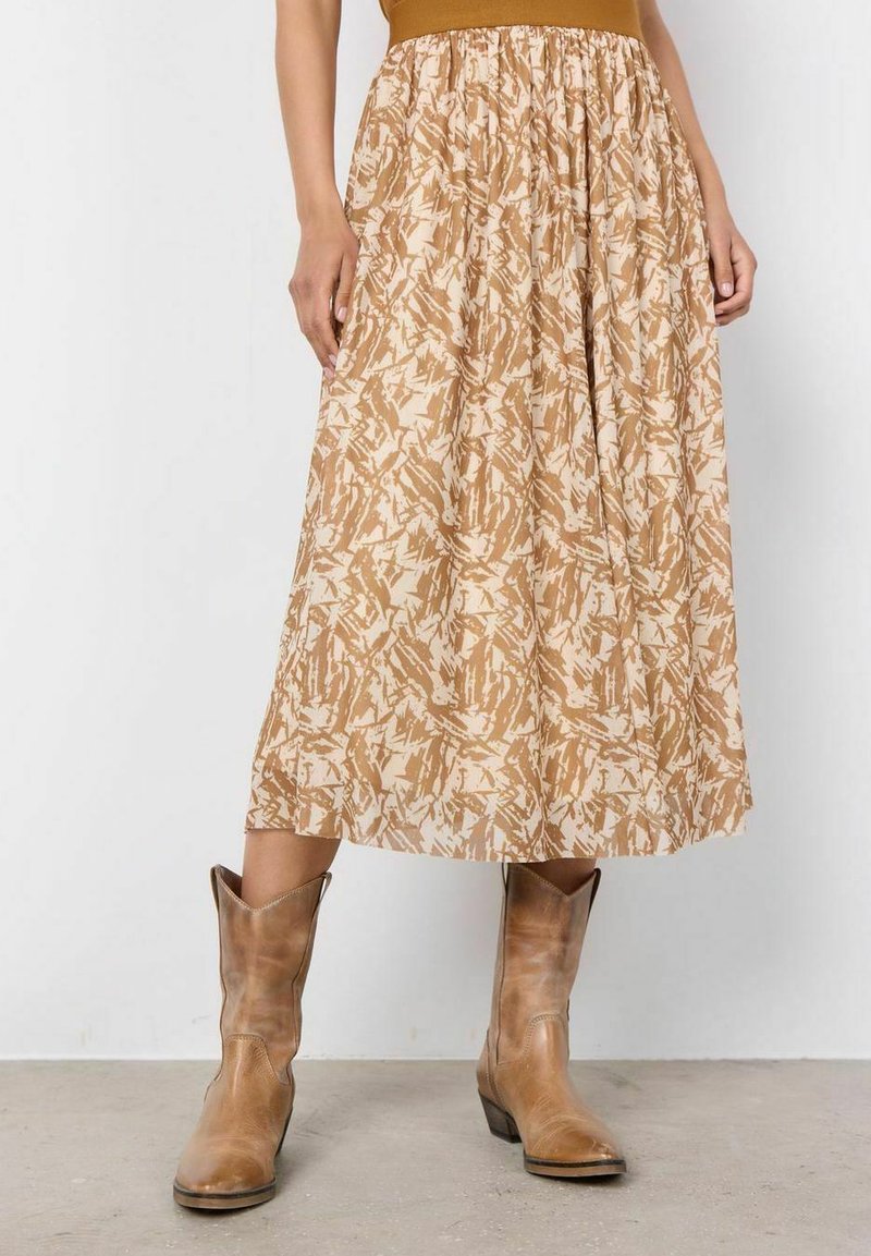 Pitkä, beige hame, jossa on teksturoitu abstrakti kuvio vaaleanruskeana. Yhdistettynä beigeihin cowboy-kengiin, joissa on koottu elastinen vyötärö.