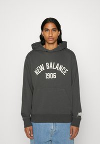 Sudadera gris con un gran estampado de "New Balance 1906". Presenta un bolsillo frontal, mangas largas y capucha con cordón. Material suave de mezcla de algodón.