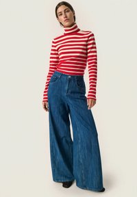Rdeče in bele prožne turtleneck pulover s širokimi modrimi jeans hlačami. Ima visok pas, sprednje žepe in sproščen kroj.