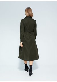 Robe longue vert olive avec une taille ceinturée, des manches longues et un col. Tissu lisse avec une silhouette fluide et longueur mi-mollet.