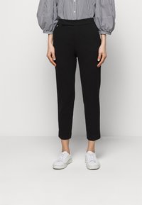 Svarta tapered-byxor i slätt tyg, med hög midja och minimalistisk design, kombinerade med vita sneakers.