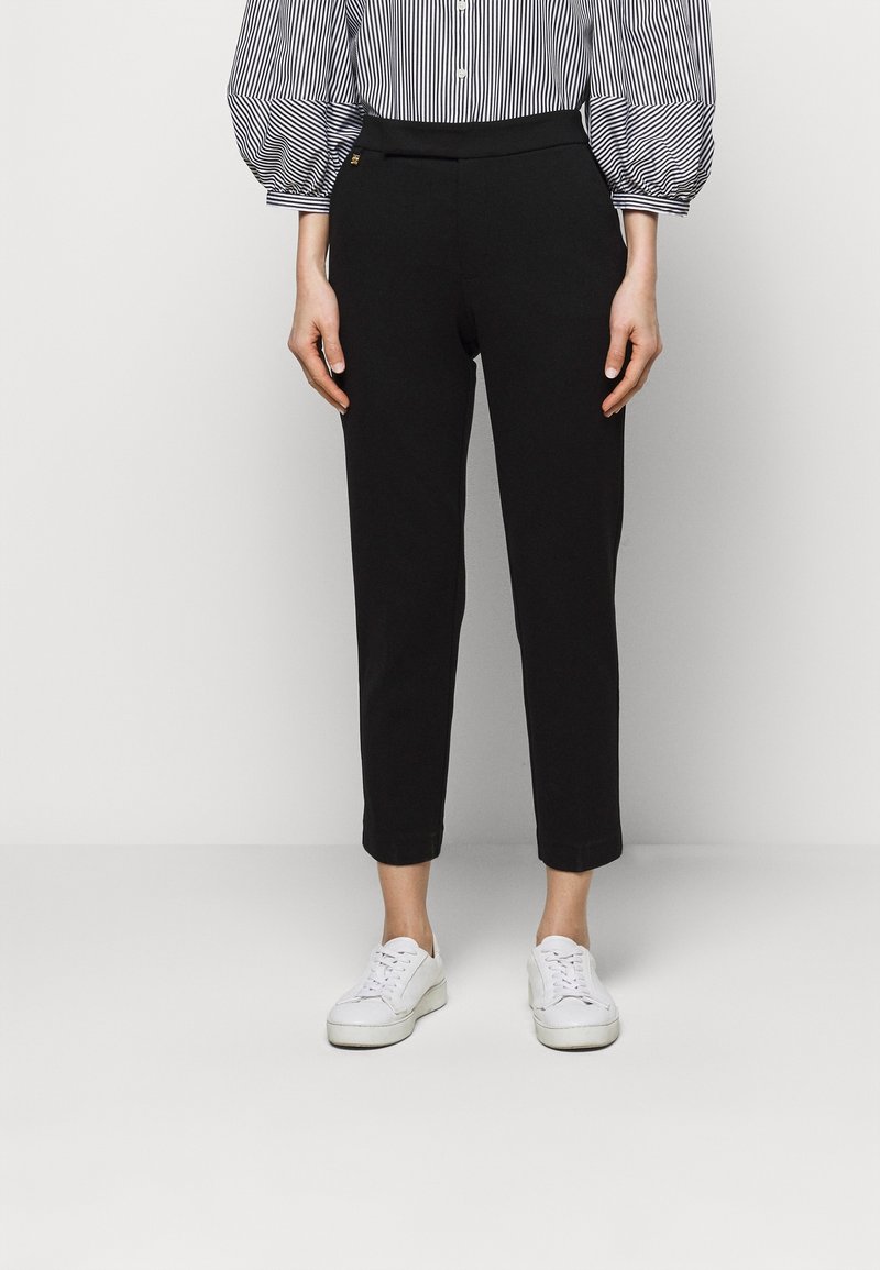 Svarta tapered-byxor i slätt tyg, med hög midja och minimalistisk design, kombinerade med vita sneakers.