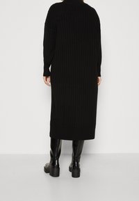 Robe tricotée noire côtelée à manches longues, longueur mi-mollet, encolure arrondie et bas ajusté. Associée à des bottes hautes noires brillantes.