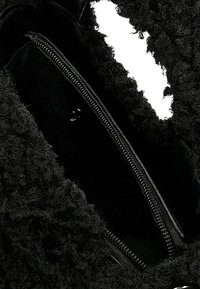 Černý chlupatý vnitřek tašky ukazující hladký, zipem uzavíratelný oddíl s měkkou texturou a kontrastní látkou v matném provedení.