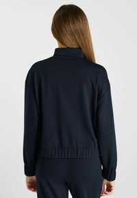 Donker marineblauwe, lichte jas met een hoge kraag, elastische manchetten en een gathered zoom. Soepele stof met een comfortabele pasvorm.