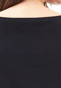 Tessuto nero, leggero di una maglietta con un ampio scollo rotondo; texture liscia; la vista ravvicinata mostra le cuciture lungo il bordo.