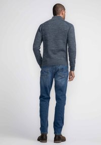 Suéter de punto gris con un cuello alto, dobladillo acanalado, combinado con jeans de mezclilla azul y botas de tobillo marrones, visto desde la espalda.