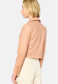 Chaqueta de cuero cortada en beige claro con cuello, costuras visibles y puños con cremallera. Textura suave y diseño ajustado.