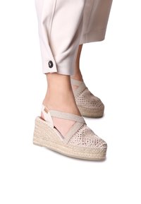Béžové espadrilové wedge sandály s pletenou jutu podešví, designem křížových popruhů a složitými tkanými detaily na svršku.