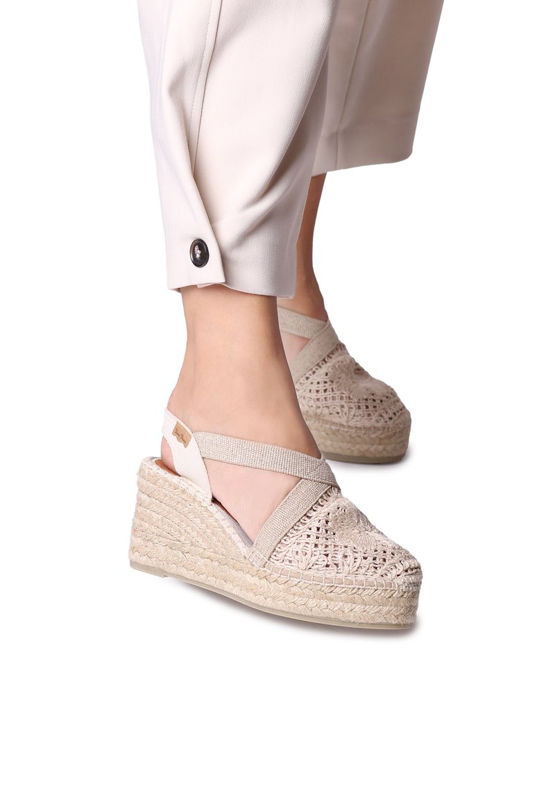 Béžové espadrilové wedge sandály s pletenou jutu podešví, designem křížových popruhů a složitými tkanými detaily na svršku.