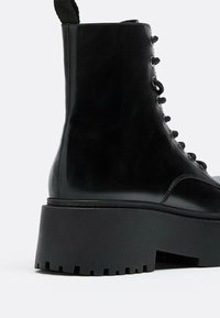 Stivale alla caviglia in pelle nera con suola spessa e zigrinata, punta rotonda e lacci frontalmente. Caratterizzato da una linguetta sul retro per una facile calzata.