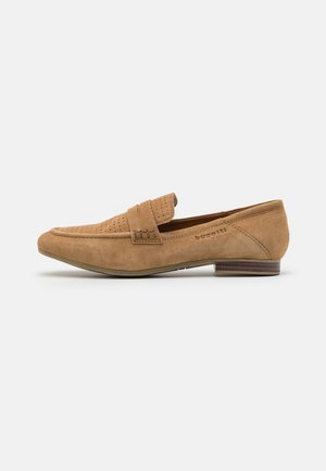 Mocasines de ante en color marrón claro con detalles perforados y una correa acolchada. Tacón plano con acentos marrones. Forma delgada y alargada.