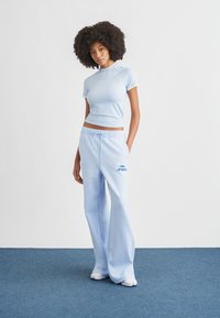 Ensemble de sport bleu clair comprenant un haut ajusté à manches courtes et un pantalon de survêtement ample avec une taille élastique et une décoration de logo.