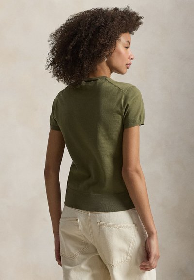 Πράσινο πλεκτό τοπ με κοντά μανίκια και στρογγυλή λαιμόκοψη, με ριμπ λεπτομέρειες στο τελείωμα, σε συνδυασμό με ανοιχτόχρωμα τζιν. Υφή υφάσματος.