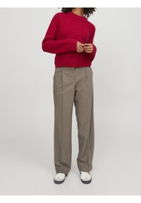 Röd stickad tröja med rund hals, i kombination med grå veckade byxor och vita sneakers. Slät konsistens med en avslappnad passform.