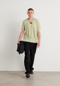 Tricou scurt cu mânecă scurtă de culoare verde deschis, cu etichetă roșie, asortat cu pantaloni negri largi și o jachetă închisă. Țesătură netedă și croială casual.