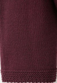 Tessuto lavorato a maglia color bordeaux con una trama a coste, bordo smerlato e motivo intrecciato all'orlo. Materiale morbido ed elastico.