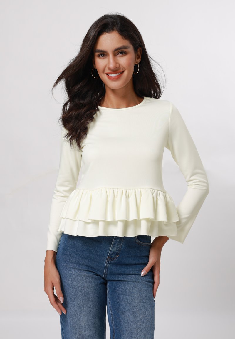 Blusa de manga larga, color amarillo claro, con un dobladillo con volantes. Textura suave, diseño ajustado, combinada con jeans azules. Cuello redondo simple.