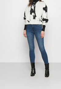 Vit och svart mönstrad sweatshirt med långa ärmar, matchad med blå smala jeans och svarta klackstövlar. Enkelt mönster, avslappnad passform.