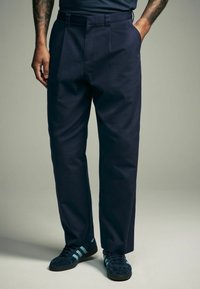 Marineblauwe broek met een recht gesneden ontwerp, voorzien van voorvouwen en zijzakken. De stof is glad met een matte afwerking.