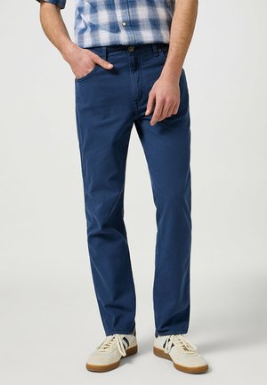Blå bomull-chino byxor med rak passform, framfickor och minimala sömmar, tillsammans med ljusa sneakers.