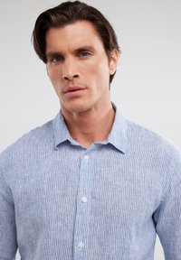 Camicia a maniche lunghe in cotone leggero con righe verticali blu e bianche. Presenta un colletto, maniche lunghe e chiusura con bottoni standard.
