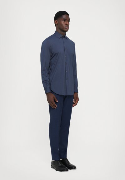 Cămașă bleumarin cu nasturi, mâneci lungi, croială slim, asociată cu pantaloni asortați, purtată cu pantofi de dress negri, textură de țesătură netedă.