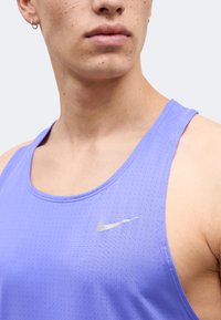 Κοντινό πλάνο ενός ατόμου που φοράει αμάνικη αθλητική μπλούζα ανοιχτό μωβ με μικρό ασημένιο λογότυπο Nike στο στήθος.