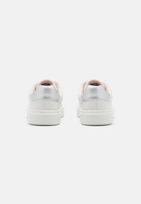White sneakers with a textured surface, silver accents at the heel, and a thick rubber sole. Rear view shows a minimalist design.