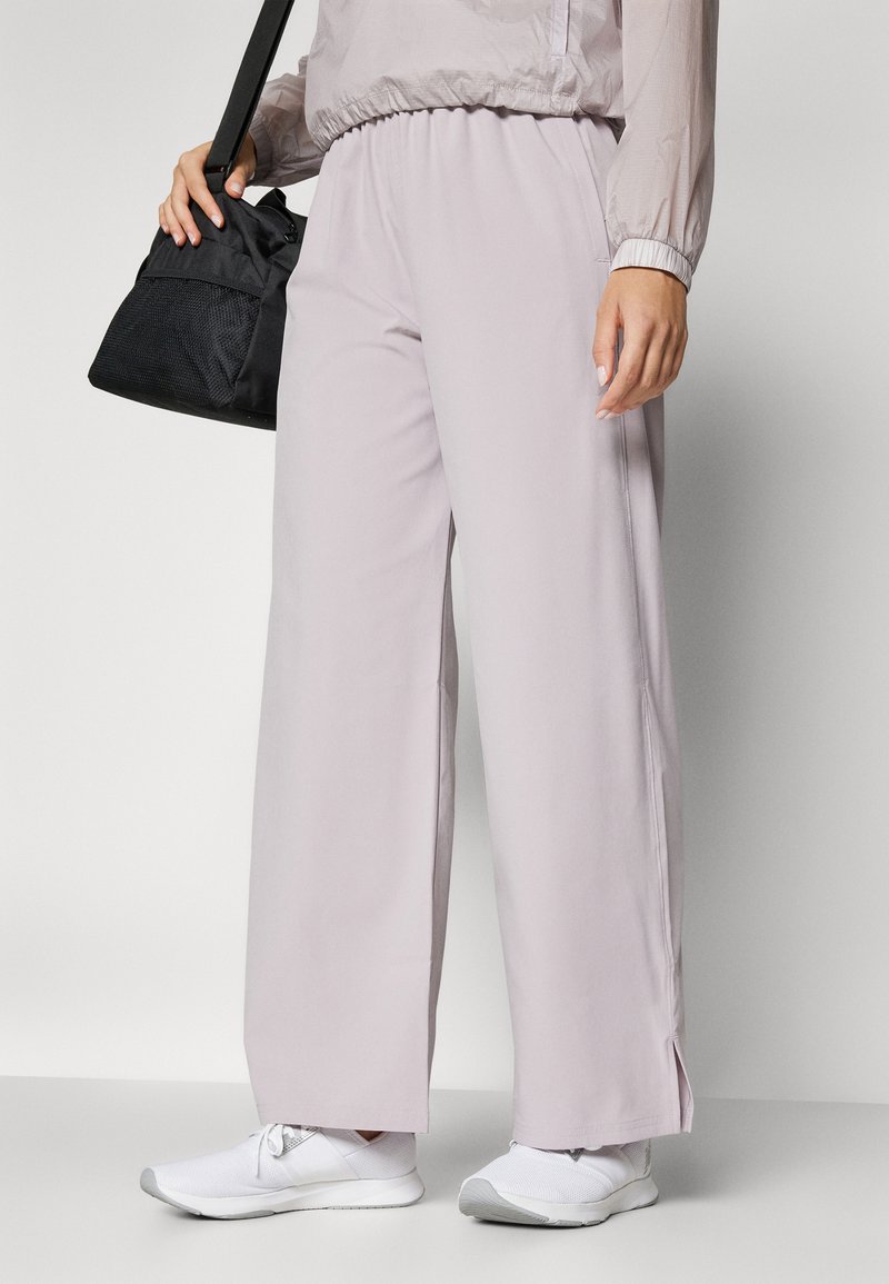 Helle mauve weit geschnittene Hose aus glattem Stoff, kombiniert mit weißen Sportschuhen, mit seitlichen Schlitzen und einem elastischen Bund.