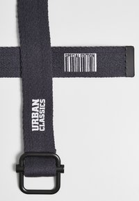 Marinevevet belte med svart hardware og trykt hvit tekst som leser "URBAN CLASSICS" og "SPECIAL EDITION." Har en rektangulær spenne.