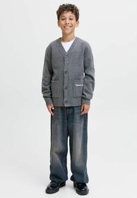 Pelēks adīts kardigans ar V-veida dekoltē, priekšējām kabatām un pogām. Apvienots ar platām, izbalējušām zilu džinsu biksēm un melniem apaviem.