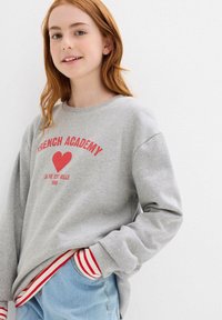 Felpa grigia con il testo rosso "French Academy" e un design a cuore, con accenti a righe rosse e bianche sui polsini e sulla vita.