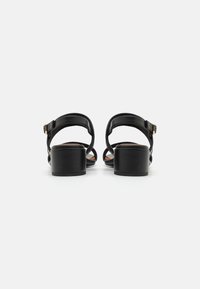 Zwarte leren sandalen met hak, met een blokhak, open achterkant en enkelband met een gouden gesp. Soepele textuur en eenvoudige silhouet.