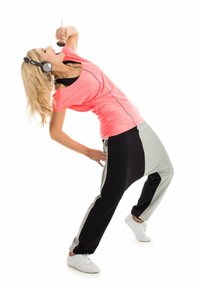 Atletska obleka, ki vključuje svetlo roza zgornji del, črno-sive hlače z raznobarvnimi bloki in bele športne copate; nosi slušalke in drži čopič za ličenje.