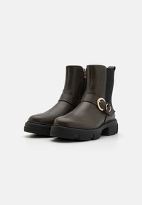 Bottines en cuir vert foncé avec une fermeture éclair latérale, un panneau élastique, une semelle noire épaisse et un accent circulaire doré sur la sangle.