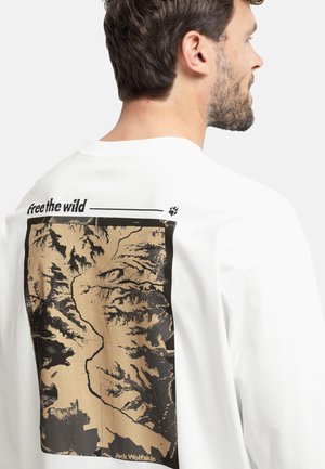 Weißes Langarm-T-Shirt mit einer großen schwarzen und goldenen Berggrafik auf der Rückseite, darüber steht "free the wild" und darunter der Markenname.