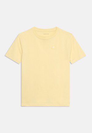 T-shirt jaune clair à manches courtes avec col rond, avec un petit patch logo Calvin Klein Jeans sur le côté gauche de la poitrine, posé à plat sur un fond blanc.