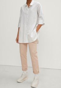 Witte blouse met lichtbeige strepen, met knopensluiting aan de voorkant en opgerolde mouwen; gecombineerd met lichtbeige cargobroek en crèmekleurige sneakers.