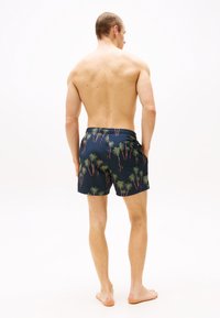 Un short de bain en tissu marine avec un motif de palmier en vert et rouge. Il dispose d'une taille élastique et de poches latérales.