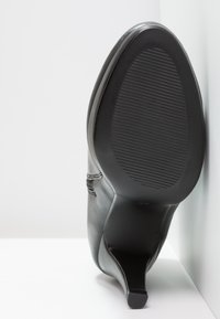 Schwarzer Leder-Stiletto mit einer strukturierten Sohle, spitz zulaufender Zehenpartie und dezenten Stichdetails entlang der Seiten, seitlich präsentiert.