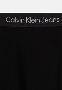 Ceinture noire avec le logo "Calvin Klein Jeans" en gris. Tissu doux et élastique avec une texture lisse, conçu pour le confort.