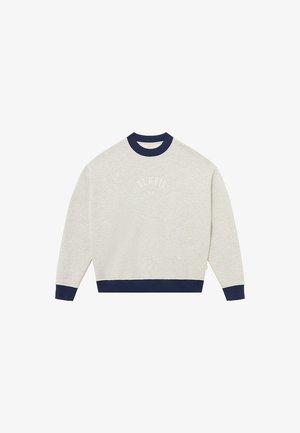 Šviesiai pilkas džemperis su tamsiai mėlynu apsiūtu apykakle ir rankogaliais. Ant krūtinės baltomis raidėmis išlenkta užrašas „BLKVLS NY“.