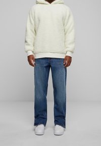 Felpa con cappuccio crema e soffice, con polsini a coste, abbinata a jeans blu a gamba dritta e sneakers bianche. Design semplice e casual.