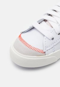 Vita sneakers med en slät läderöverdel och gråa mockadetaljer samt klara orange sömmar. Texturerad gummisula med snörning.