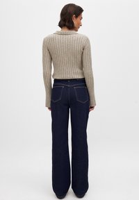 Beige ribbad tröja med förlängda ärmar, som matchas med mörkblå vida jeans med bakfickor och kontrasterande sömmar.