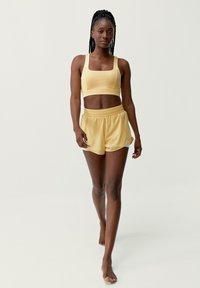 Sujeción deportiva amarilla y pantalones cortos a juego, fabricados con una tela suave y ligera. El sujetador tiene un escote cuadrado; los pantalones cortos cuentan con una cinturilla elástica.