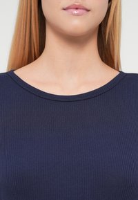 Top bleumarin cu dungi, decoltat rotund, dintr-un material moale, cu o textură netedă și un design mulat.